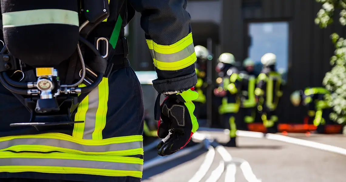 Feuerwehrmann in Uniform, im Hintergrund Feuerwehrmänner im Gespräch