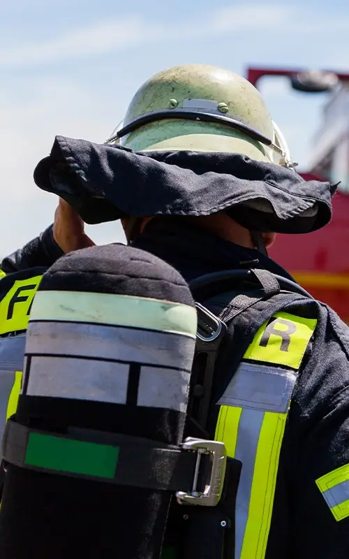 Feuerwehrmann mit Sauerstoffflasche auf dem Rücken hält sich den Helm